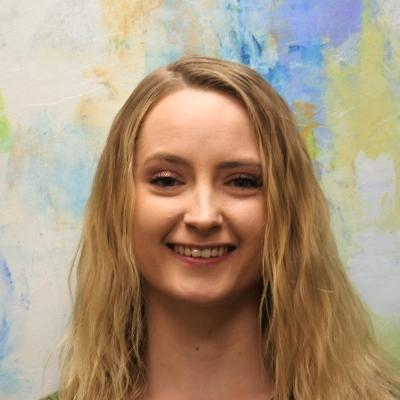 Chiropractic Assistant Annie Frost Smiling In Front Of Watercolor Painting