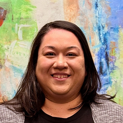 Front Desk Manager Crystal Meno Smiling In Front Of Watercolor Painting