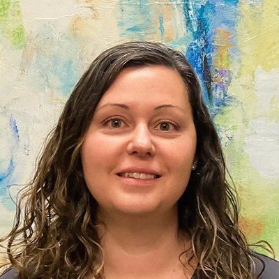Front Desk Manager Crystal Tharpe Smiling In Front Of Watercolor Painting