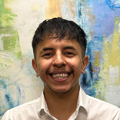 Physical Therapist Assistant Gustavo Mosqueda-Cuellar Smiling In Front Of Watercolor Painting