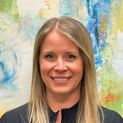 Physical Therapist Jaime Darling Smiling In Front Of Watercolor Painting