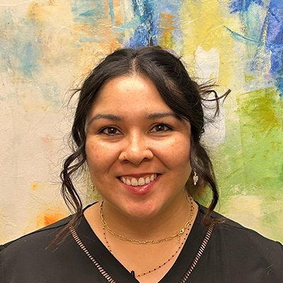 Licensed Massage Therapist Janelle Muñoz Smiling In Front Of Watercolor Painting