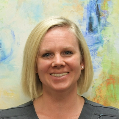 Licensed Massage Therapist Kaalyn Norvell Smiling In Front Of Watercolor Painting