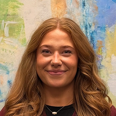 Chiropractic Assistant Kali Carlson Smiling In Front Of Watercolor Painting