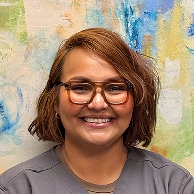 Licensed Massage Therapist Kristin Valdez Smiling In Front Of Watercolor Painting