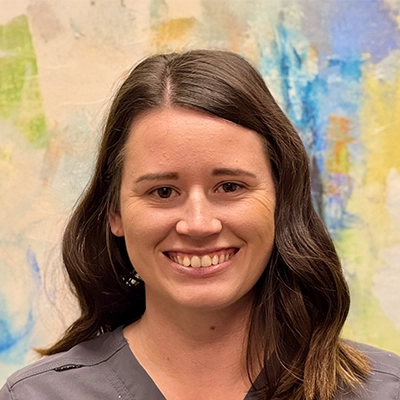 Chiropractic Assistant Taylor Sullivan Smiling In Front Of Watercolor Painting