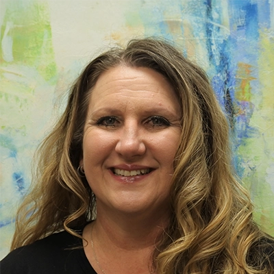 License Massage Therapist Tracy Frazier Smiling In Front Of Watercolor Painting