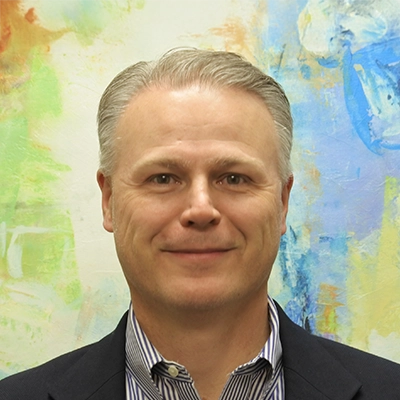 Chiropractor Chad Abercrombie Smiling In Front Of Watercolor Painting