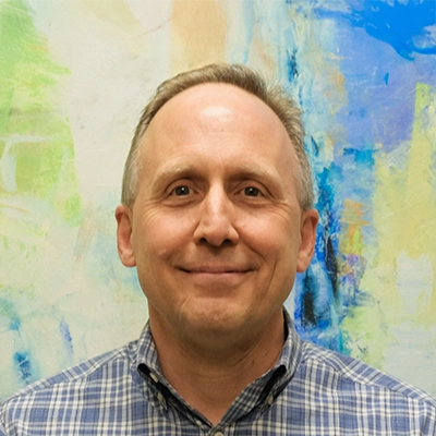 Chiropractor James Thatcher Smiling In Front Of Watercolor Painting